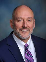 This is a picture of Joe Morrissette. He is a white male wearing a white dress shirt, blue suit coat and purple, blue and white tie.